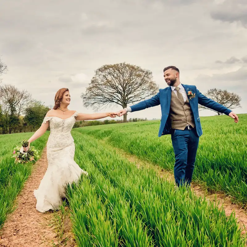 Newlyweds holding hands in a Worcestershire meadow